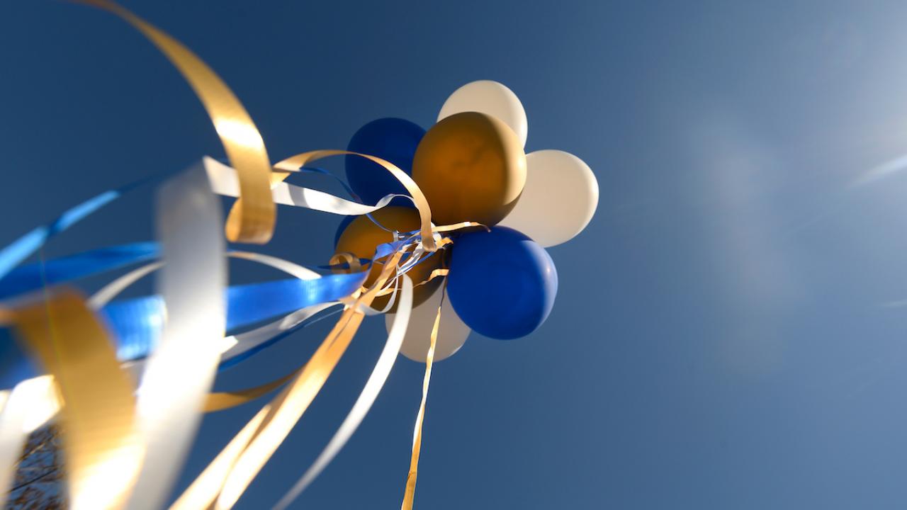 celebratory blue, gold, and white balloons with a deep blue sky